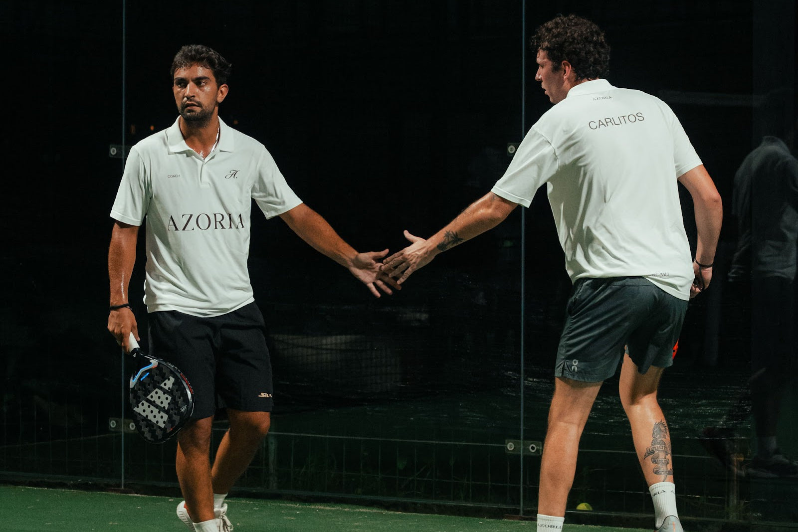 Two padel players in Azoria kit touching hands between points on court in Uluwatu, Bali